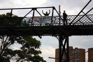  Local residents hang a Clean Train Coalition banner on the Wallace Ave. pedestrian bridge.