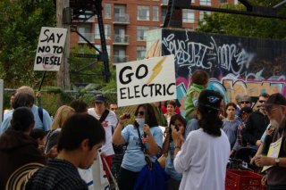  A protester carrying a "Go Electric" placard under the Wallace Ave. pedestrian bridge.